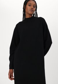 Vestito maglione oversize nero con collo alto e maniche lunghe, realizzato in tessuto morbido, caratterizzato da un design minimalista senza pattern.