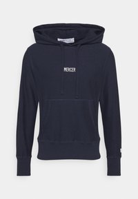 Hoodie bleu marine en tissu doux, avec une poche kangourou, des poignets en côtes et un cordon de serrage. Logo "MERCER" en blanc sur le devant.