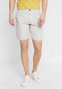 Světle šedé bavlněné šortky s knoflíkovým uzávěrem, poutky na opasek a bočními kapsami. V kombinaci s jednoduchým žlutým tričkem a bílými teniskami.