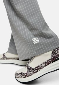 Graue Nadelstreifenhose mit einem Etikett am Saum, kombiniert mit weißen und leopardenmuster Sneakern mit schwarzen Sohlen und Mesh-Akzenten.