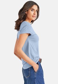 Lichtblauwe T-shirt met korte mouwen, gemaakt van zacht materiaal, met een relaxte pasvorm en opgerolde mouwen. Draag het met donkere denim jeans.