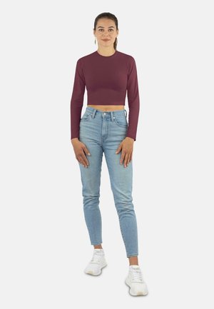 Bordeauxrotes, kurz geschnittenes Langarmoberteil kombiniert mit hellblauen, hochtaillierten Jeans und weißen Sneakers. Der Stoff wirkt glatt und hat einen figurbetonten Schnitt.