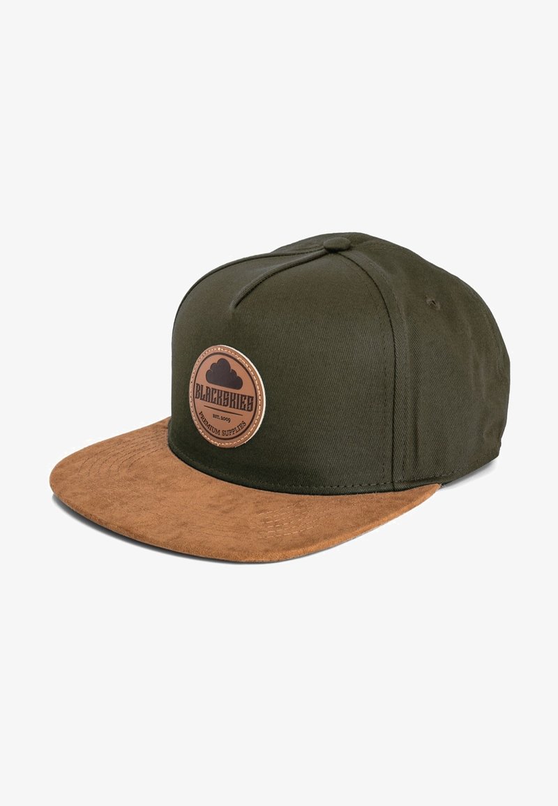 Gorra verde oliva con visera de ante marrón. Presenta un parche circular de cuero con texto. Detalles cosidos en la corona y la visera.