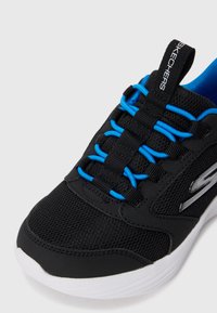 Nærbilde av svart Skechers-sneaker med blå elastiske lisser, mesh-overdel og hvit såle på hvit bakgrunn.