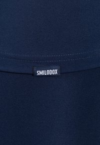 Tessuto sportivo blu navy con una texture rigata, dotato di un'etichetta nera con la scritta "SMILODOX" cucita saldamente sul materiale.