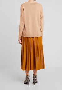 Beige pletený svetr s volným střihem, kombinovaný s plisovanou midi sukní v hořčicově žluté barvě a texturovanými šedými kotníkovými botami.