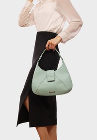 Borsa a mano in pelle verde chiaro con forma strutturata, dotata di una patta superiore piatta e di un manico corto, arricchita da dettagli in metallo argentato.