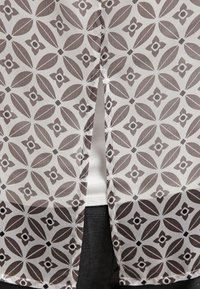 Tessuto trasparente con un motivo floreale ripetuto in tonalità di marrone e crema. Presenta uno spacco sul retro e una texture liscia.