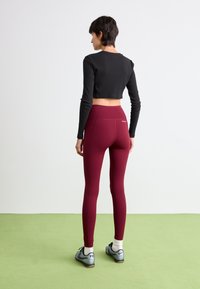 Svart kortärmad topp med långt ärm, som är kombinerad med högmidjade vinröda leggings, som har en slät textur och diskret branding på baksidan.