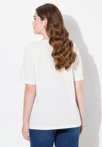 Hvid t-shirt med korte ærmer lavet af blødt stof, med rund halsudskæring og en afslappet pasform, iført mørkeblå jeans.