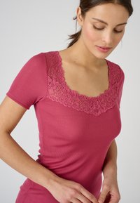 Haut ajusté à manches courtes en rose avec un col en dentelle florale appliquée. Texture lisse, design classique et col en forme de scoop.