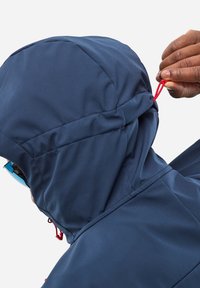 Veste imperméable bleu marine avec capuche ajustée, montrant une main ajustant un cordon rouge. Présente une texture lisse et des coutures renforcées.