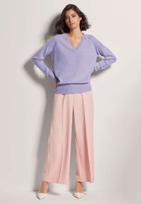 Lavender-V-Ausschnitt-Pullover mit gerippten Bündchen, kombiniert mit rosa weit geschnittenen Hosen und weißen spitzen Absätzen. Glatte Stoffqualität mit lockerer Passform.