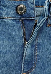 Jean en denim bleu avec fermeture éclair métallique partiellement ouverte et bouton argenté fixé à la taille avec des coutures visibles.