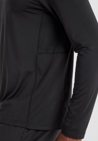 Long-sleeve black athletic top made of smooth, stretchy fabric. Features a textured mesh panel on the side and flatlock seams for comfort.