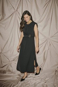 Robe noire sans manches avec une ceinture à la taille au motif circulaire. Détail fente sur le côté, accompagnée de ballerines noires à bout pointu. Tissu doux.