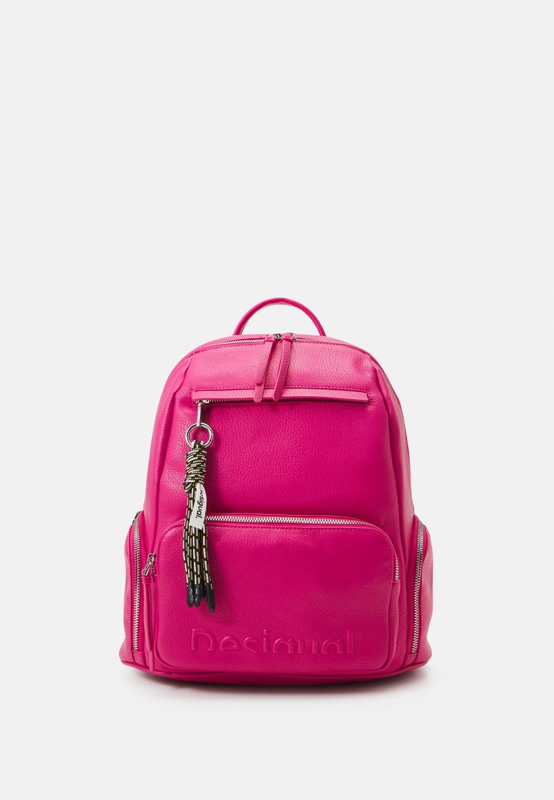 Sac à dos rose vif avec plusieurs poches zippées et un porte-clés pompon tressé noir et blanc accroché à la fermeture éclair de la poche avant.
