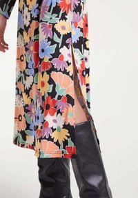 Vestido floral de largo medio con abertura lateral que revela botas de cuero negras hasta la rodilla sobre un fondo claro.