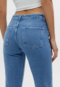 Jean en denim bleu clair avec une taille haute, deux poches arrière et une texture lisse. Le design est simple avec une coupe classique.