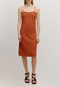 Rood-gemêleerde gebreide jurk met een chevronpatroon, spaghettibandjes, knielange snit, gecombineerd met bruine sandaaltjes met bandjes.