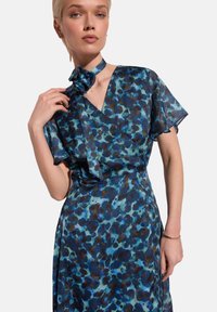 Kwiatowa niebiesko-turkusowa sukienka z krótkimi falbaniaste rękawami, dekoltem w serek oraz dopasowanym wiązaniem z tkaniny przy szyi. Lekka, lekko przezroczysta struktura.