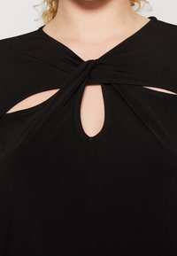 Top nero con design annodato e ritagli sulcollo e ai lati. Realizzato in un materiale liscio e elastico.