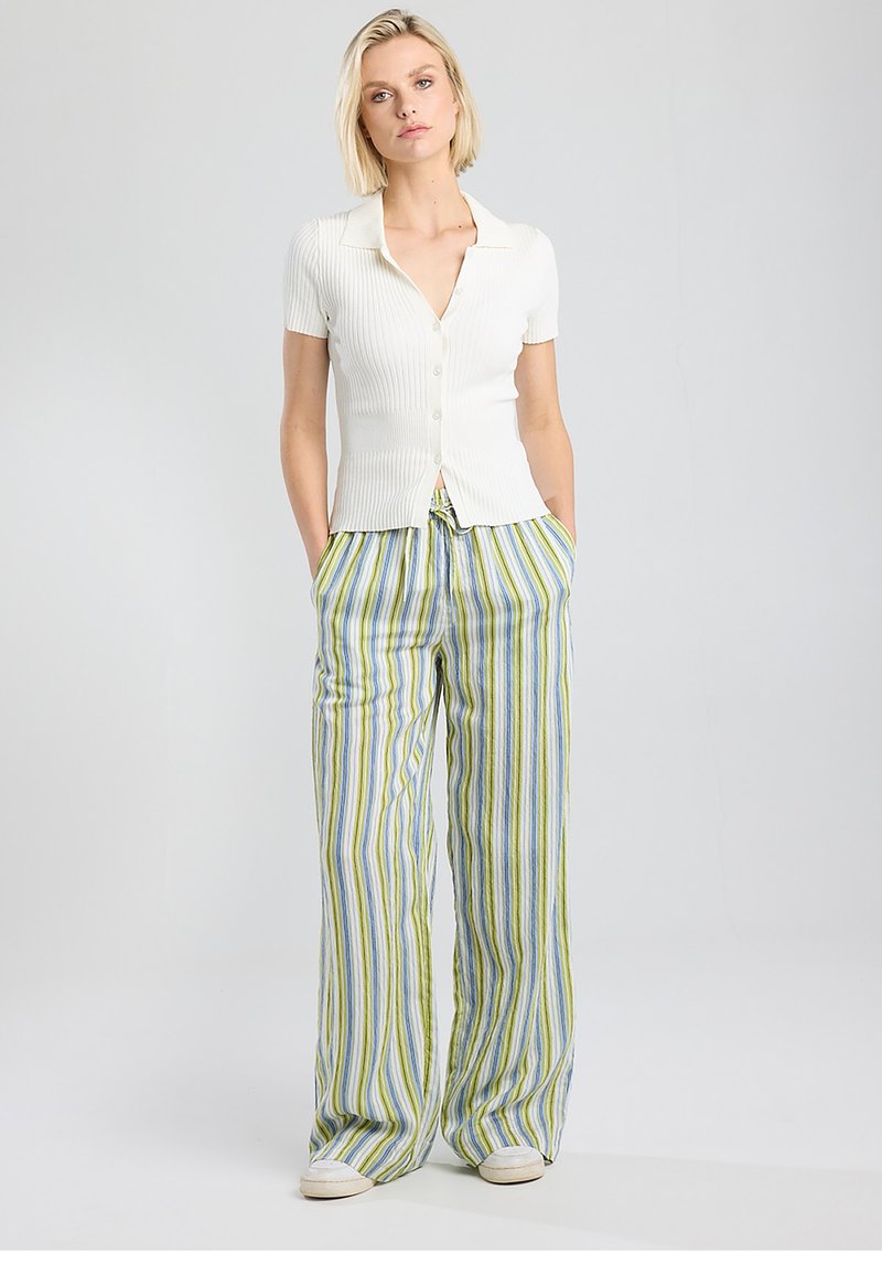 White ribbed short-sleeve button-up top paired with loose, multicolored striped pants in green, blue, and white. Casual fit with pockets.