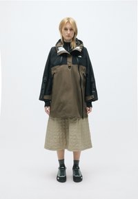 Ūdensizturīgs pulovers jaku melnā un brūnā krāsā, ar iezipināmu priekšpusi, sānu kabatām un kapuci. Saskaņota ar quiltētu beżīgu svārku un melnām kurpēm.