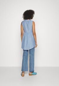 Túnica sem mangas, azul e branca às riscas, com uma cintura franzida, acompanhada de tamancos azuis claros e jeans azuis de cintura alta.
