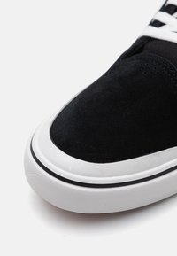 Fekete velúr sneaker fehér gumitalppal és fekete díszítéssel, sima felsőrésszel és kontrasztos fehér fűzőkkel. Lekerekített orr kialakítás.