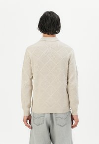 Suéter de punto beige con un patrón de diamantes, con un cuello y puños de canalé, textura ligera y un ajuste relajado.
