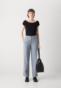 Black fitted top, light blue wide-leg trousers with front pockets, and chunky black shoes. Holding a black bag with a shoulder strap.