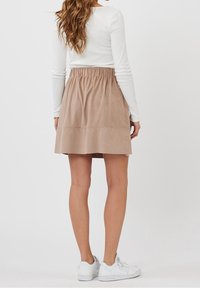 Jupe en daim beige avec une taille élastique, longueur genou, présentant une texture lisse et de légères coutures horizontales. Assortie à des chaussures blanches.