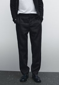 Black linen trousers with a tailored fit, featuring a flat front and side pockets, paired with black loafers and a white t-shirt.