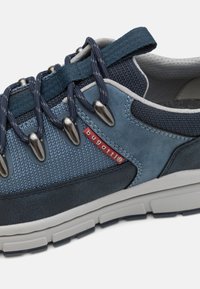 Baskets décontractées bleu et marine avec semelle blanche épaisse, œillets métalliques, lacets marins, et petite étiquette rouge portant l'inscription "bugatti" sur le côté.