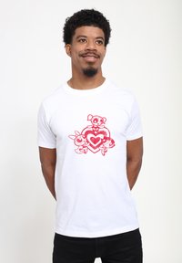 Witte katoenen t-shirt met een rood grafisch ontwerp waarop drie cartoonfiguren binnen een hart zijn afgebeeld. Korte mouwen en een ronde hals.