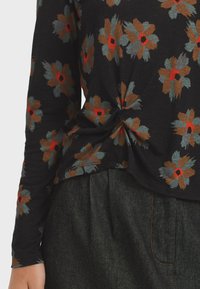 Black long-sleeve top with brown, gray, and red floral patterns, featuring a front twist detail, paired with dark gray pants.