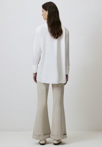 Witte lange mouwen shirt met een afgeronde onderkant, gecombineerd met beige flared broeken. Glad materiaal met een ontspannen pasvorm, zichtbare manchetten en elegante schoenen.