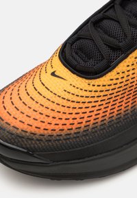 Nike juoksukengät, joissa on orange ja musta verkko-yläosa, jossa on gradienttiefektin muotoilu, teksturoitu pinta mustilla yksityiskohdilla ja nyörityssuljenta edessä.
