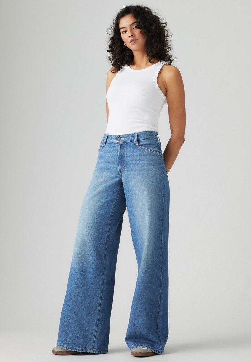 Jeans a vita alta in denim chiaro a gamba larga, con un lavaggio sbiadito. Abbinati a un top fitted senza maniche bianco.