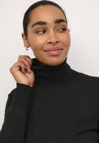 Must värviga kõrge kaelusega turtleneck-sviiter, mis on valmistatud pehmest kudumiskangast ning millel on soonikuline tekstuur ja istuv disain. Peened detailid hõlmavad kõrget kaela.