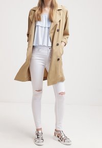 Tan trench coat, ljusblå volangtop, vita rivna skinny jeans och silverfärgade gladiatorsandaler. Mjuk textil; avslappnad passform.