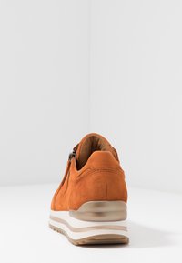 Rostfärgad mockasko med vit plattformssula och siddragkedja, visad bakifrån på en helt vit yta.