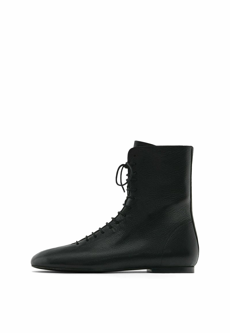 Bottes noires en cuir avec une finition texturée, dotées d'un bout pointu et d'un devant à lacets. La semelle est plate et au design minimaliste.