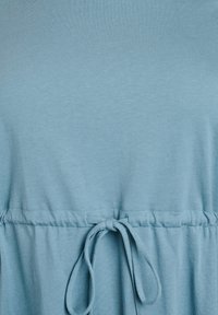 Robe t-shirt bleue en tissu doux, dotée d'une taille ajustable par cordon et d'une texture lisse. Design simple sans motifs ni accents.