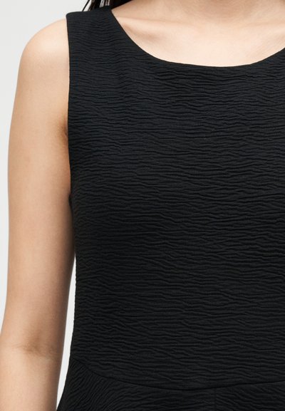 Αμάνικο μαύρο φόρεμα με υφή κυματιστό μοτίβο υφάσματος, που φοριέται από άτομο με ανοιχτό τόνο δέρματος.