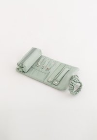 Ljusgrön accessoarpåse i slätt tyg. Har en zippered fack, flera tryckknapps-stängningar och ett samlat elastiskt band.