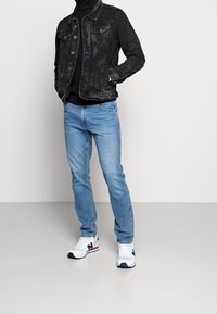 Svart denimjacka med två framfickor, bärs över en svart polotröja. Matchas med ljusblå jeans och vita sneakers med marinblå accenter.