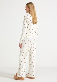 White pajama set with repeating teddy bear print, featuring long sleeves and loose-fitting pants. Soft fabric and relaxed design.