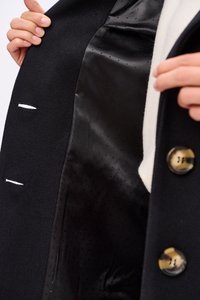 Czarna marynarka z gładką, czarną satynową podszewką, z białymi szwami i złotymi guzikami. Materiał ma teksturowane sploty.